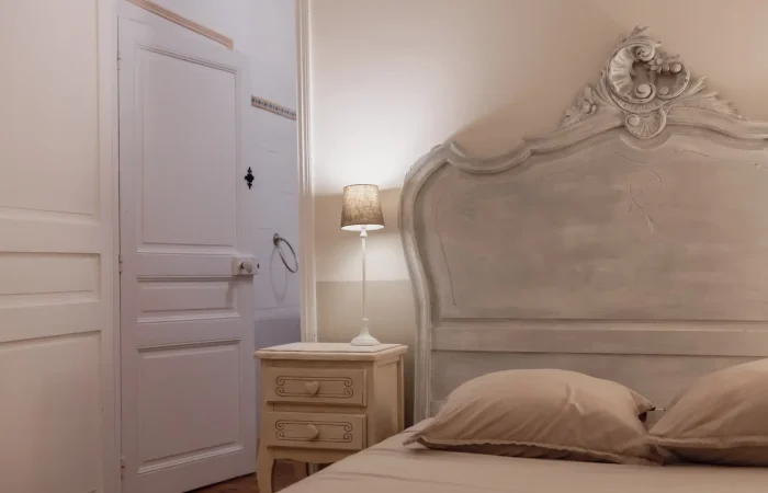 Suite Artemis au Parc de Lesseps — détail tête de lit baroque en bois patiné, chevet provençal, lumière douce, hébergement de charme pour week-end romantique ou mariage en Indre