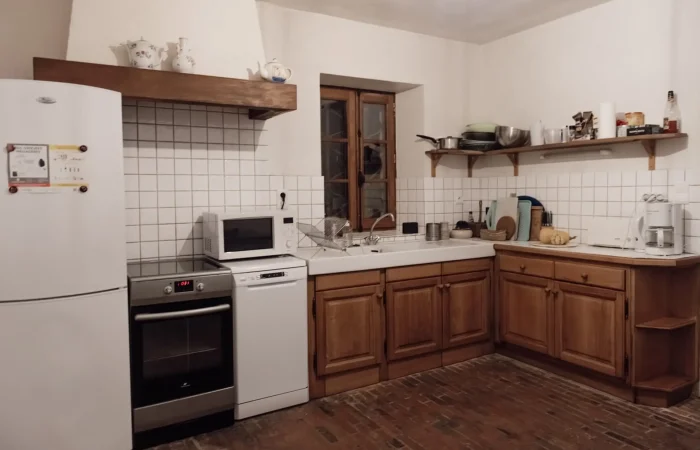 Cuisine équipée du gîte Le Presbytère au Parc de Lesseps — meubles en bois massif, hotte en pierre, tomettes, four et lave-vaisselle, cadre authentique pour séjour en famille ou week-end de mariage en Berry