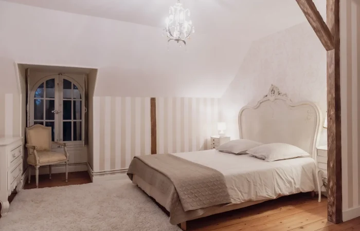 Suite Diane du gîte Le Presbytère au Parc de Lesseps — lit baroque blanc, fenêtre en arche, poutre apparente, lustre en cristal, chambre double idéale pour nuit de noces ou séjour romantique en Indre