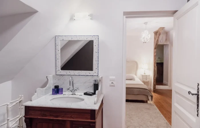 Salle de bain de la suite Diane au gîte Le Presbytère — vasque sur meuble en bois, plan en marbre blanc, vue sur la chambre baroque, hébergement de caractère en Berry